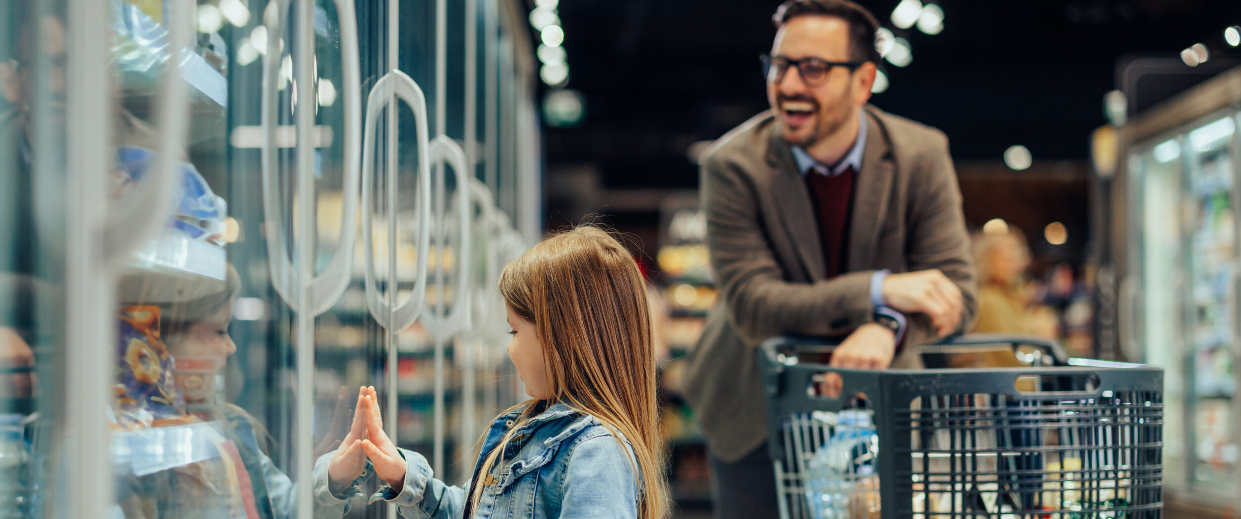A little girl is showing her dad ice cream in the supermarket fridge