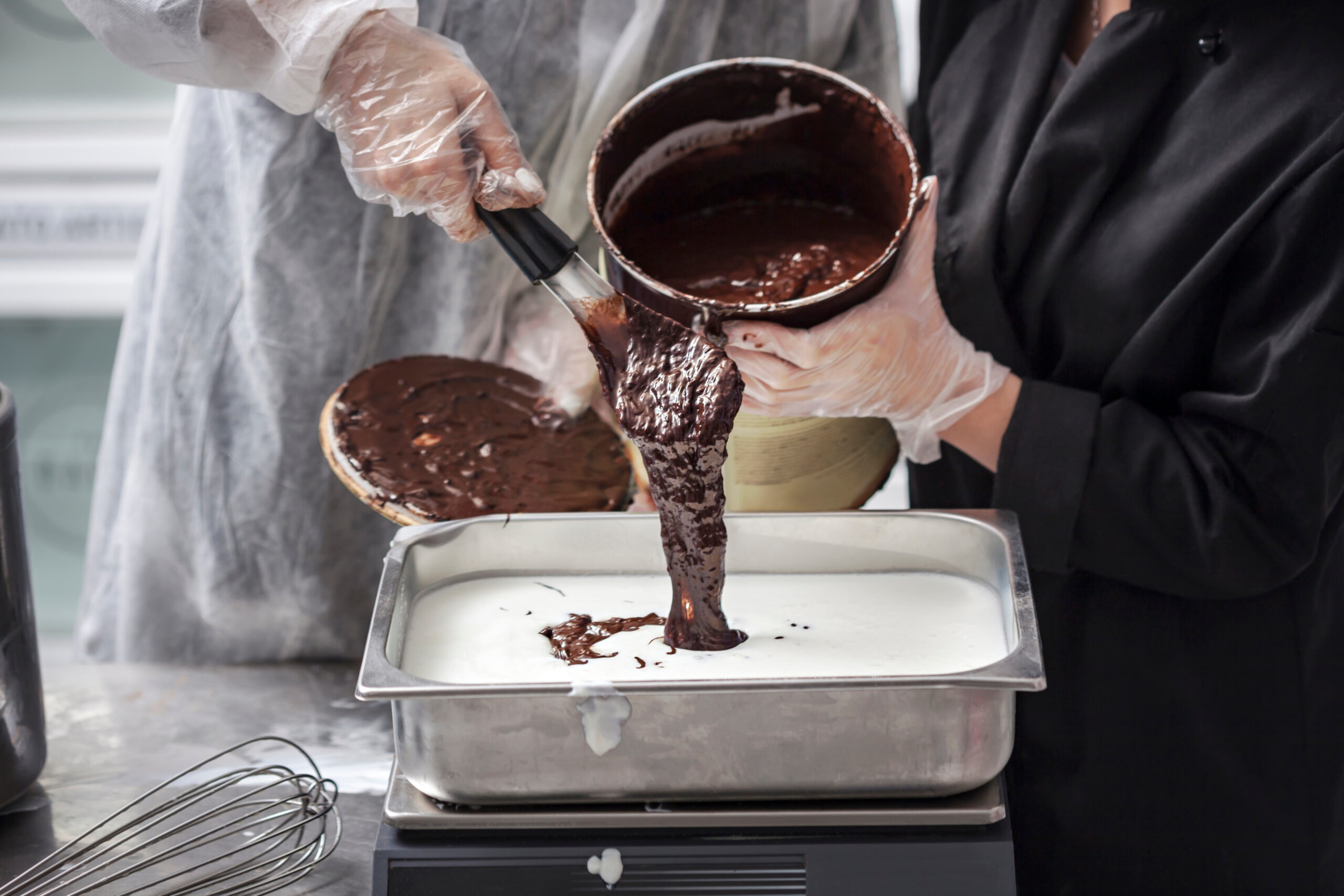 Women hands in gloves preparing chocolate ice cream - pouring chocolate ganache in stainless steel tray