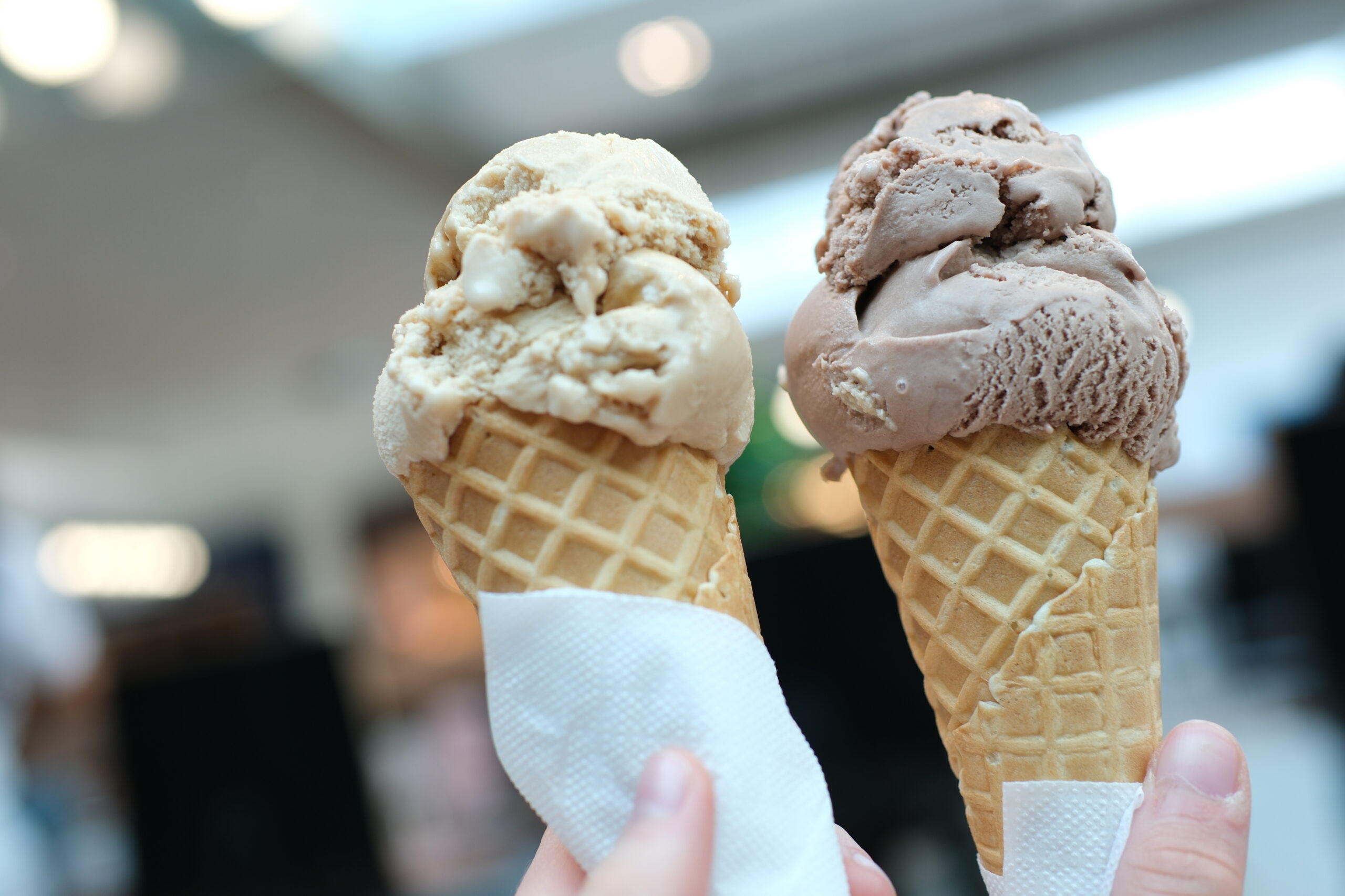 Two servings of ice cream cone on background of Mall, two girls clinking together with a brown and light dessert, like glasses, game of communication, Friendship, eating delicious dessert.
