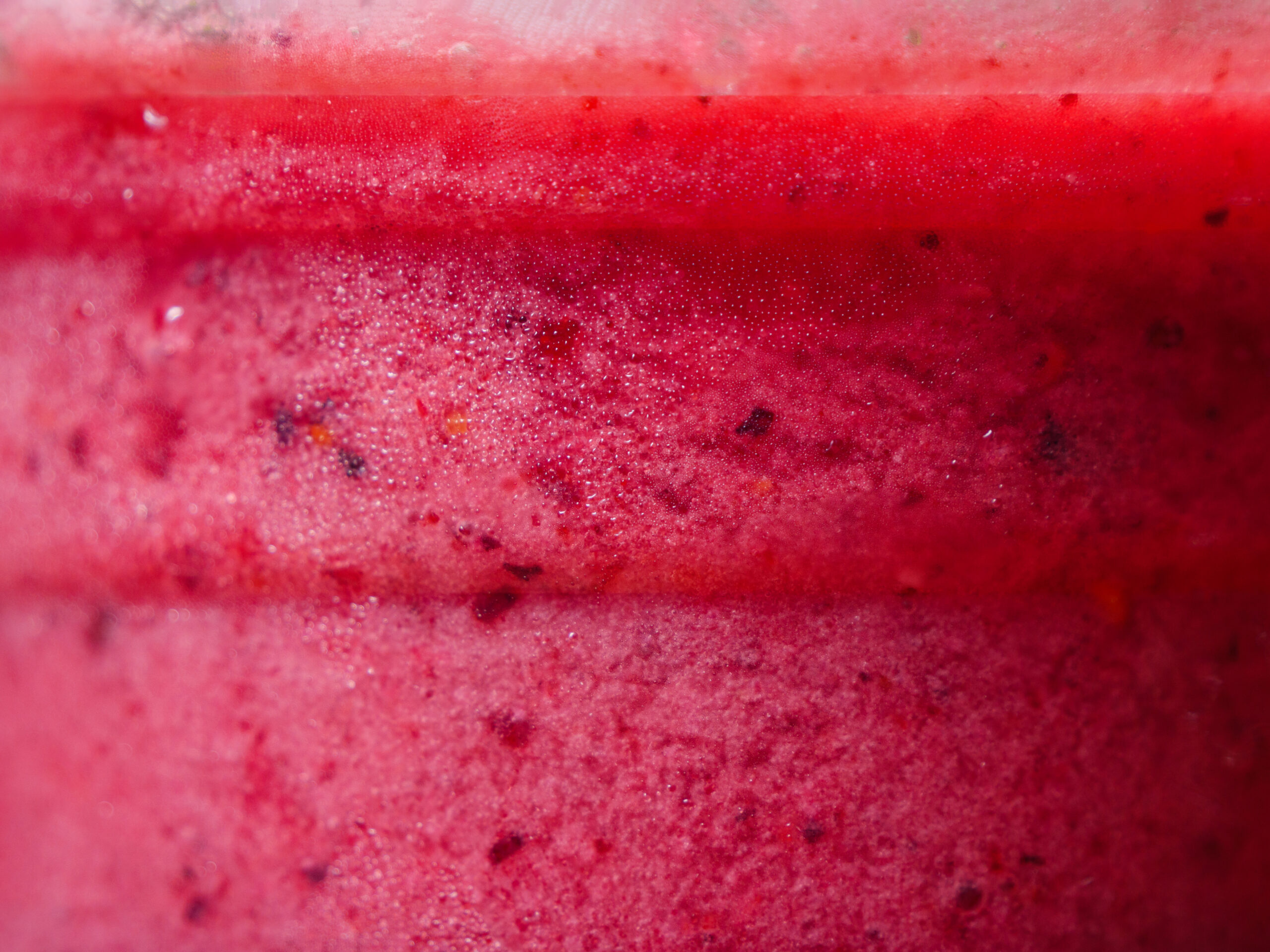 A macro shot of a pink red berries smoothie in a cup, showcasing its detailed texture and vibrant color.