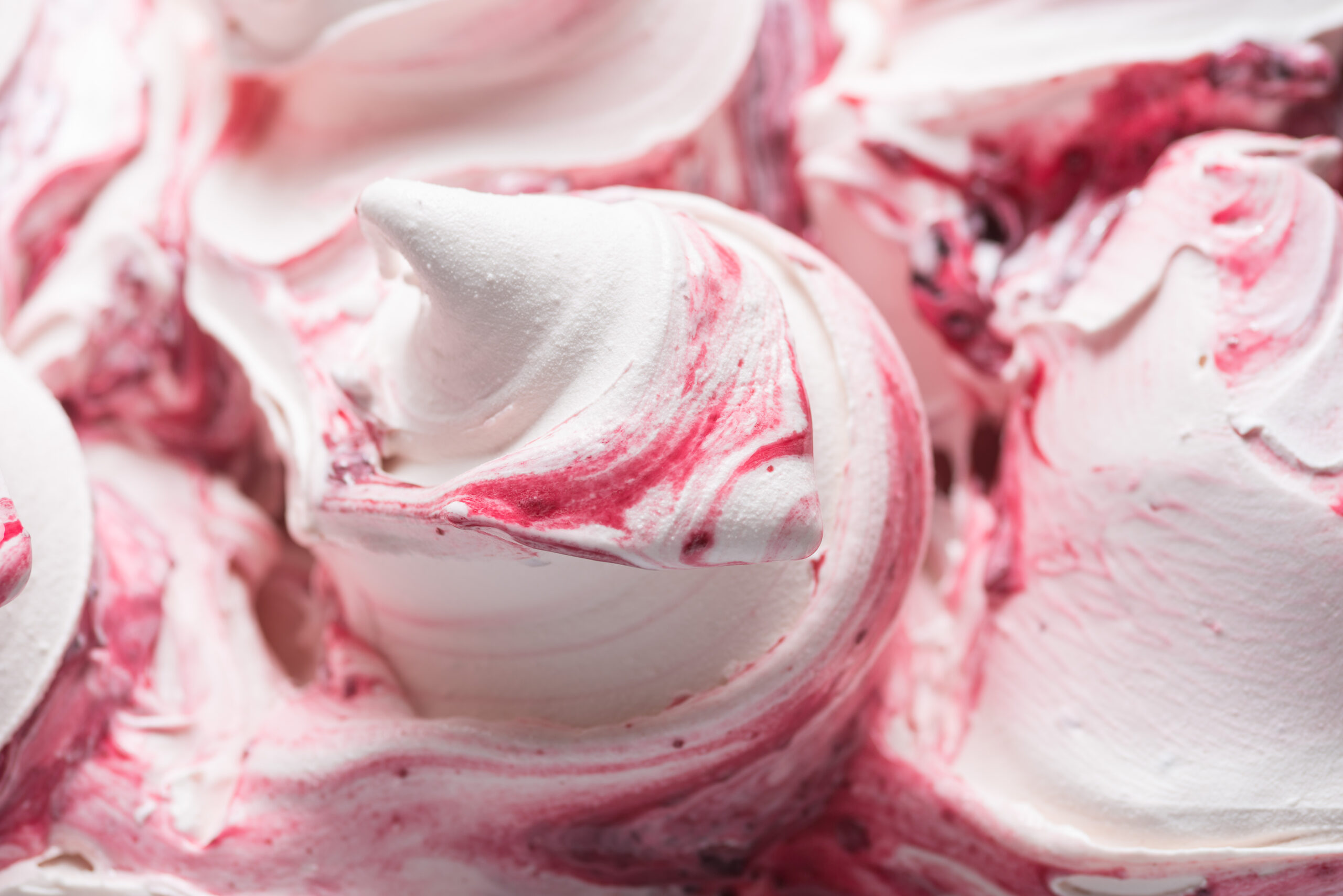 Close-up of fruit-swirled ice cream base showing smooth, shelf-stable texture - Frozen Cherry flavour gelato - full frame detail. Close up of a white surface texture of Ice cream covered with red swirls.