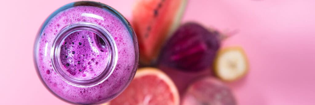 Top view of a bright purple fruit smoothie surrounded by fresh fruit, showing globally inspired finished beverage applications.