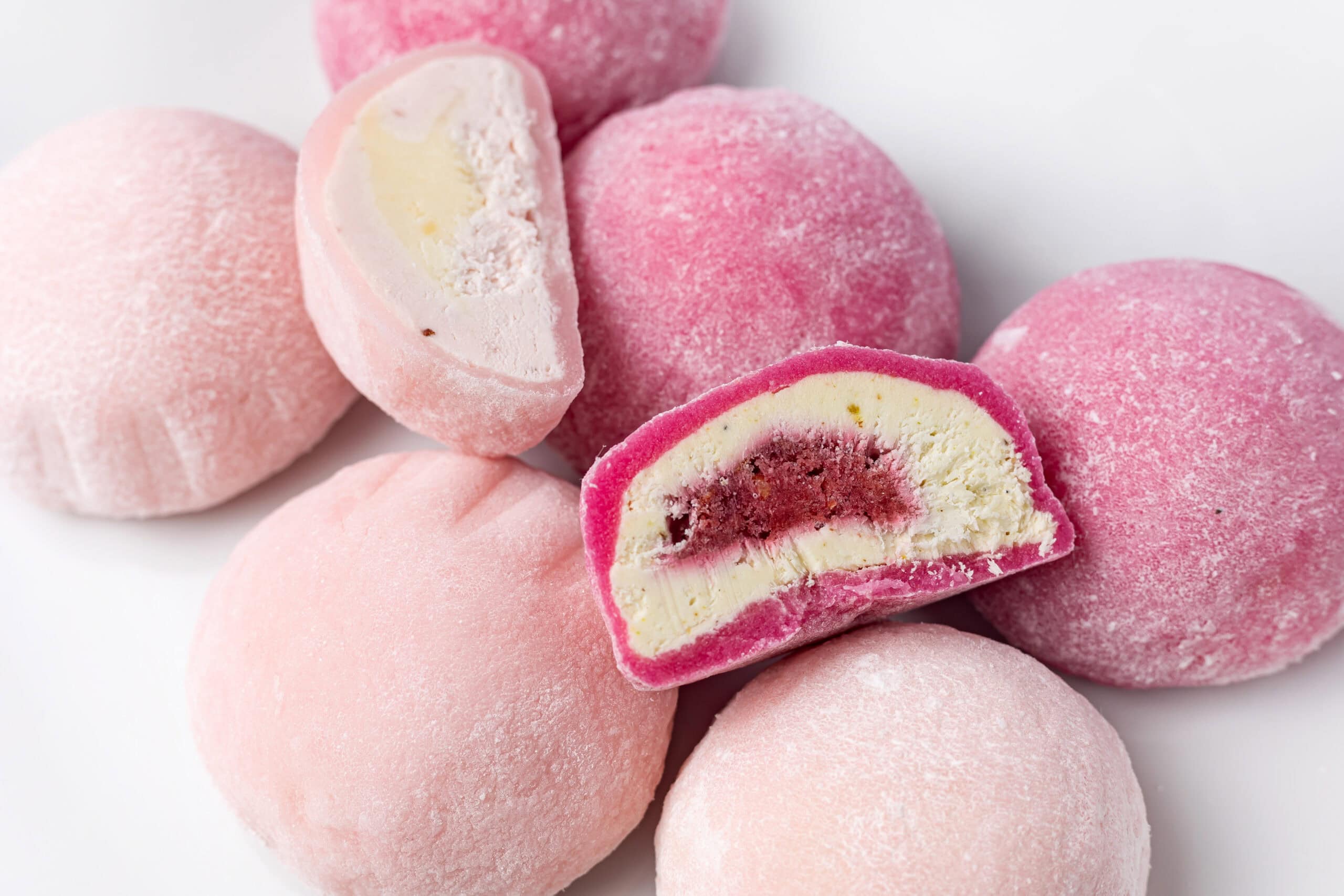 Pink mochi ice cream bonbons with one cut in half revealing creamy vanilla interior with berry filling, demonstrating Asian-inspired chewy texture innovation