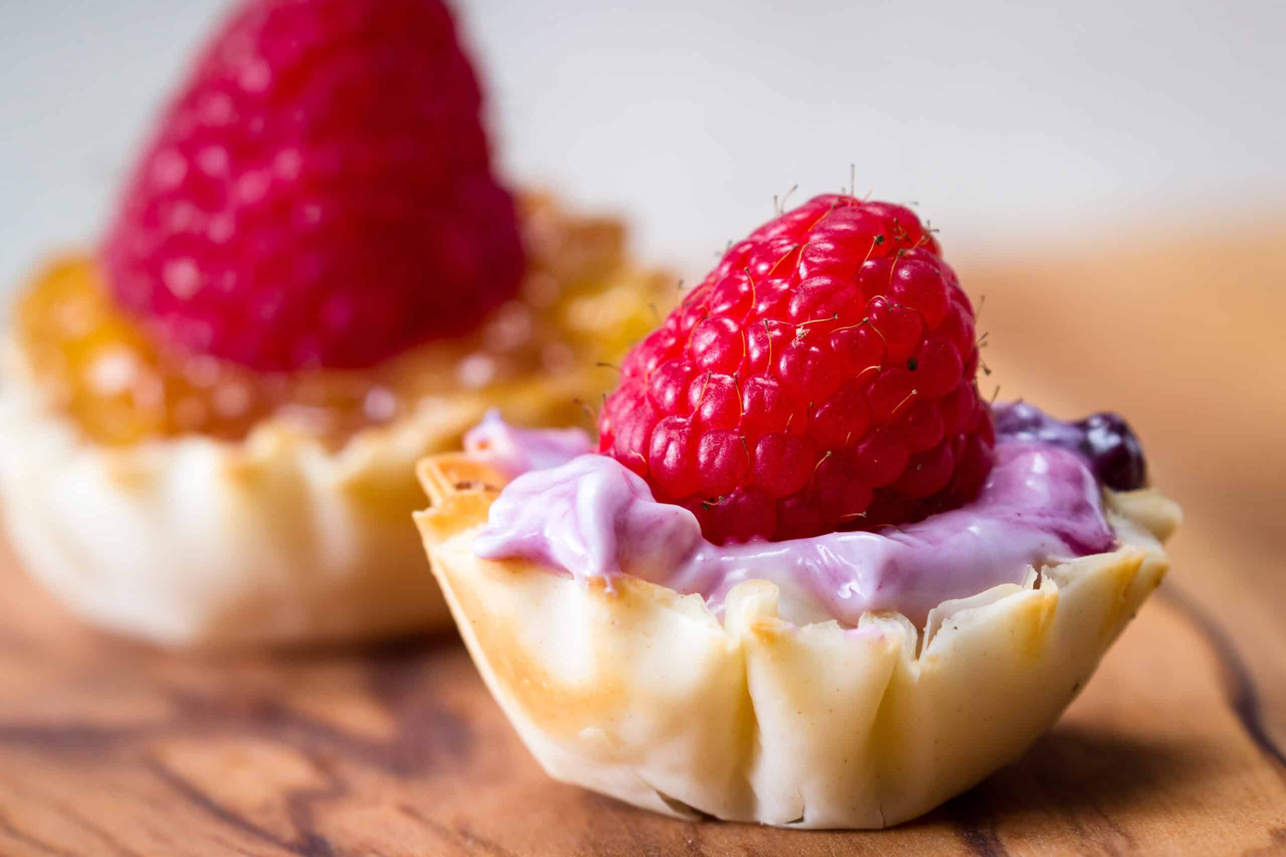 Individual tartlet with fresh raspberry and creamy filling representing premium, portion-sized