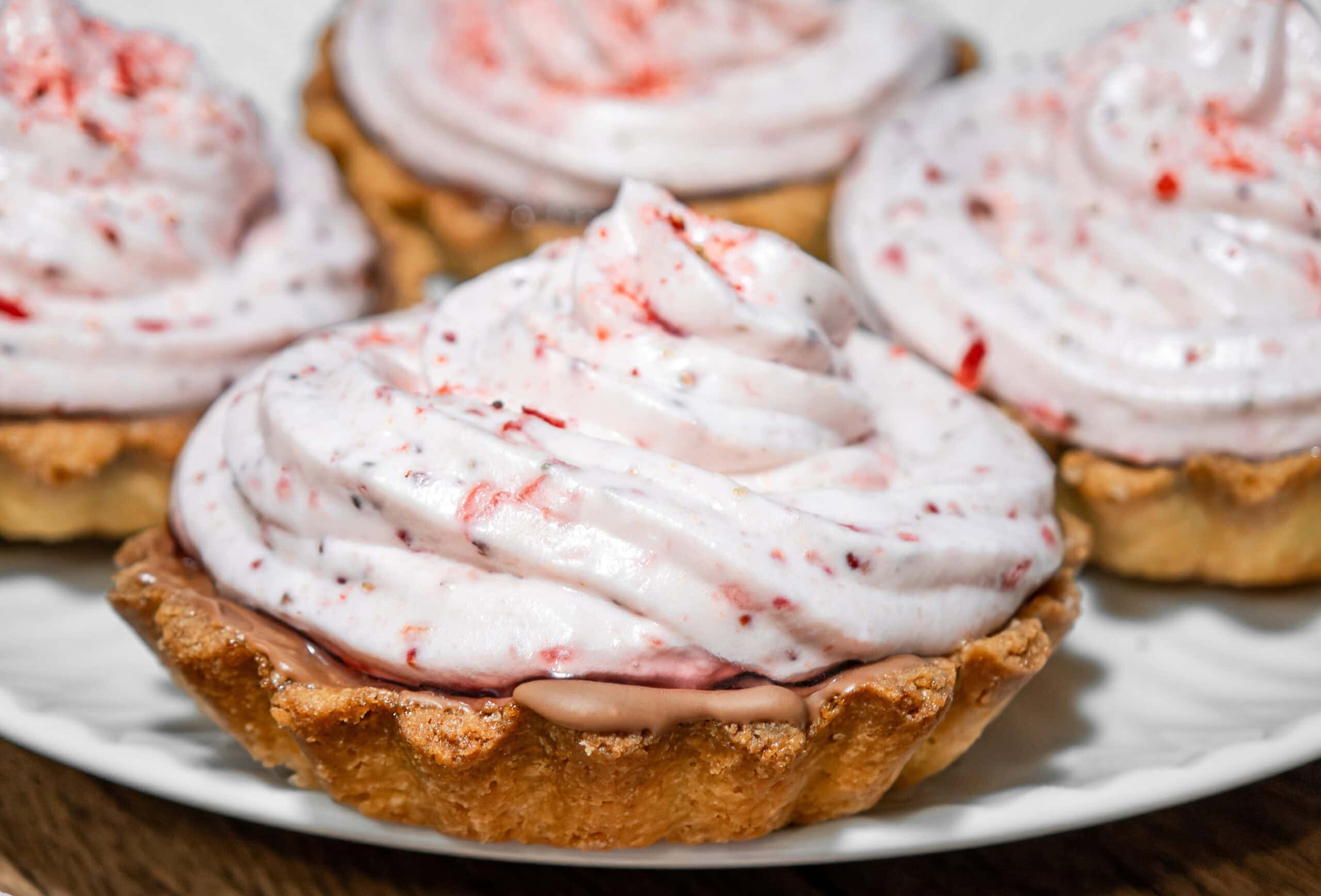 Individual strawberry tartlets with piped frosting and fresh berry garnish representing premium, portion-sized baked goods