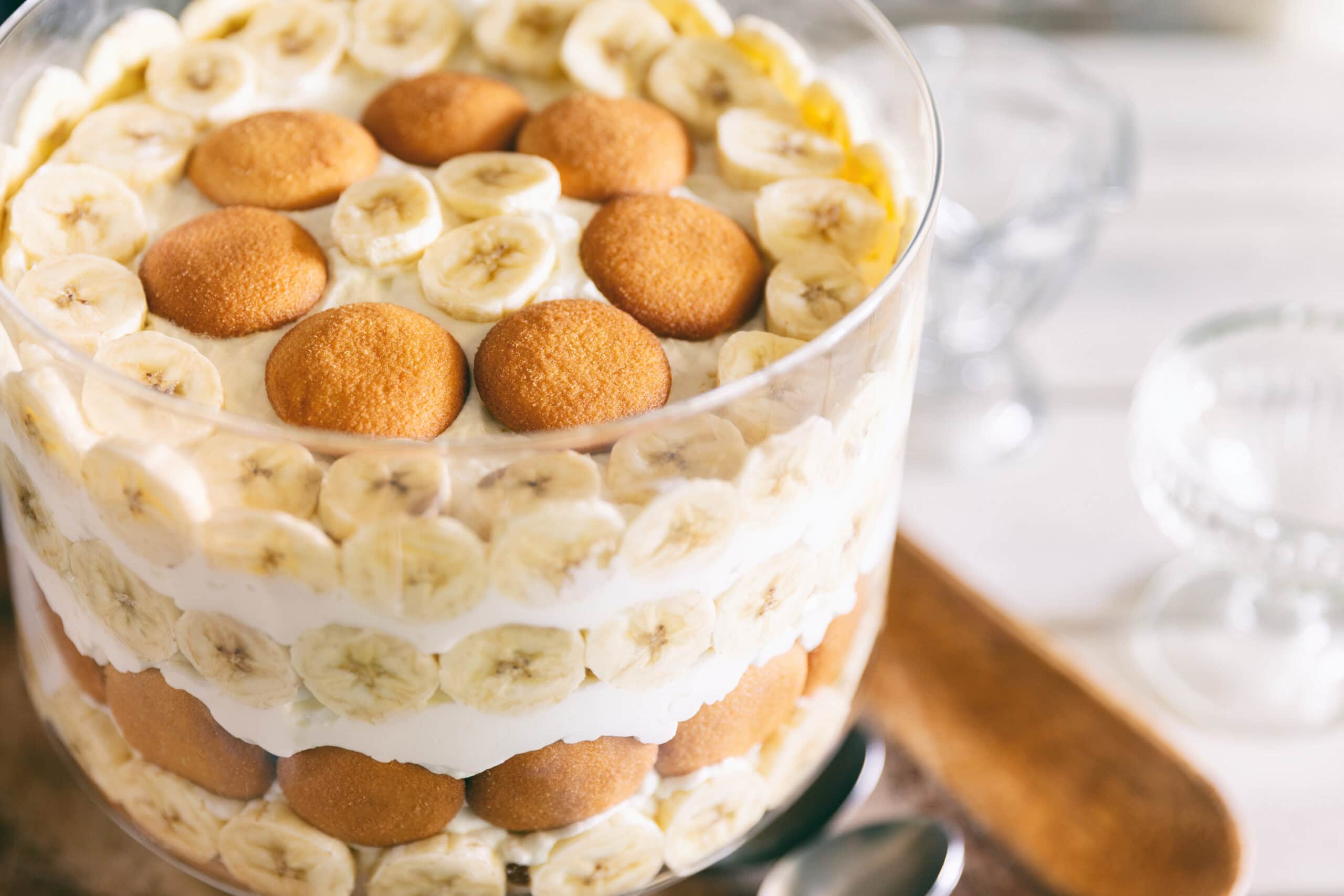 A layered banana pudding trifle in a large glass bowl with rows of vanilla wafers, fresh banana slices, and cream