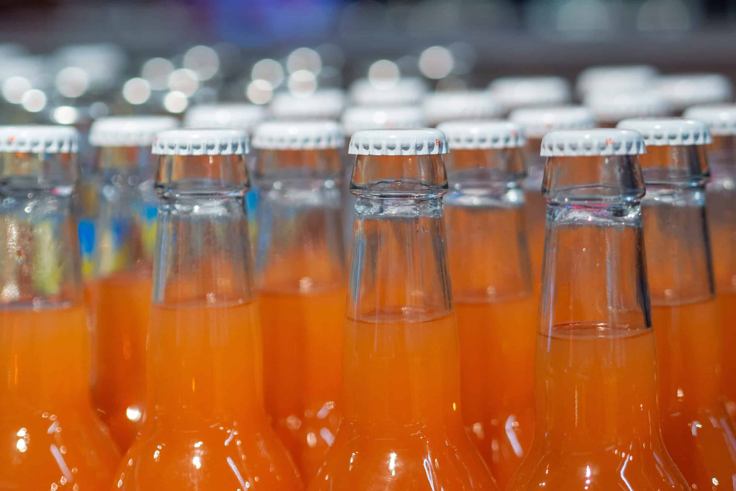 Rows of nostalgic glass bottles filled with orange flavor soda lined up in a classic retro style