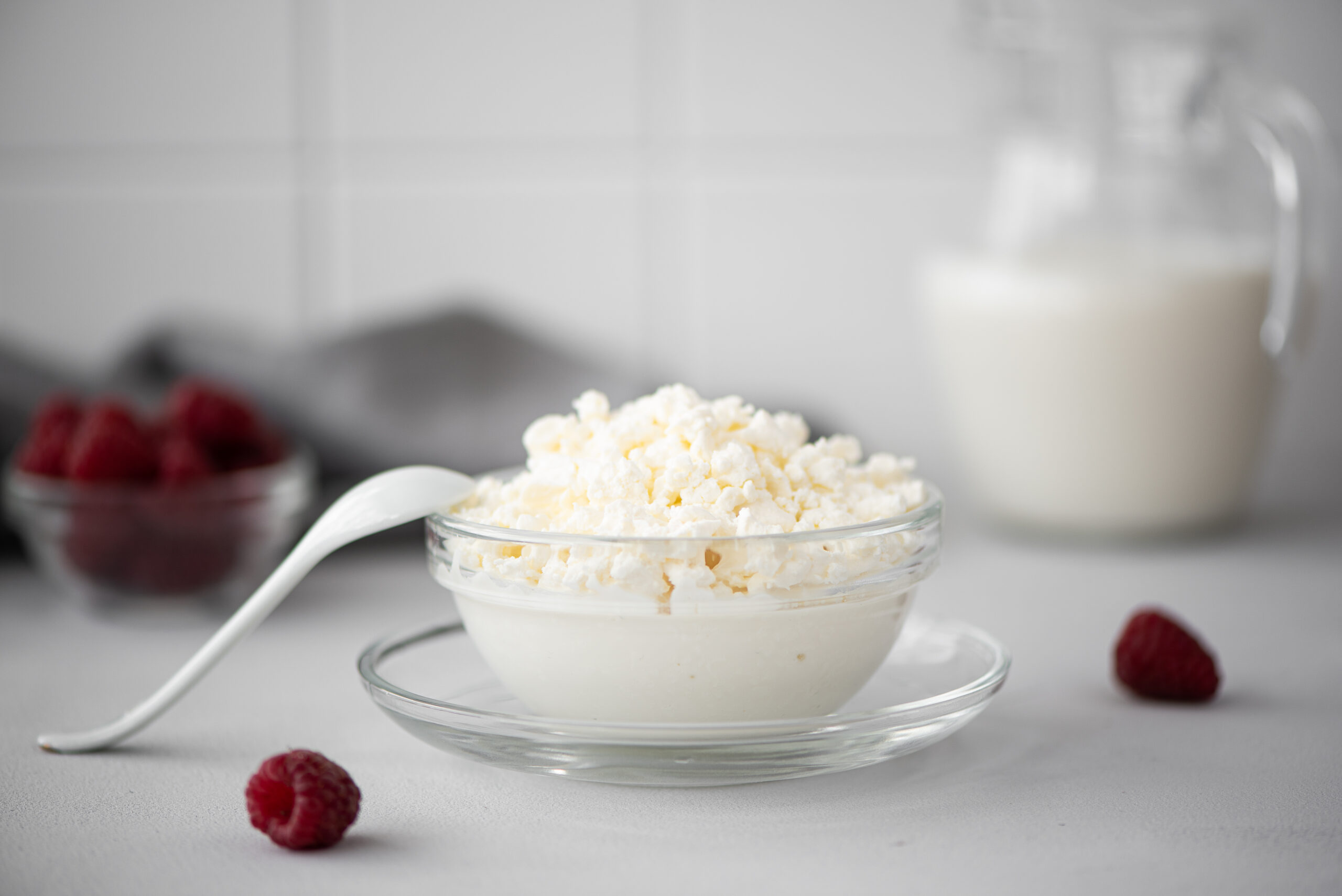 Fresh cottage cheese in a glass bowl with raspberries and a milk pitcher on a light surface representing the cottage cheese protein trend
