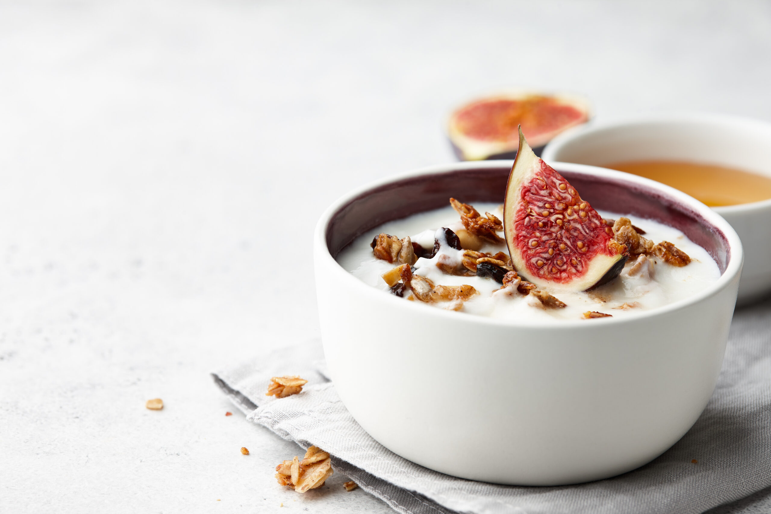 Bowl of creamy yogurt topped with fresh fig slices, granola, and a side of honey on a light linen surface showcasing premium flavor innovation in cultured dairy