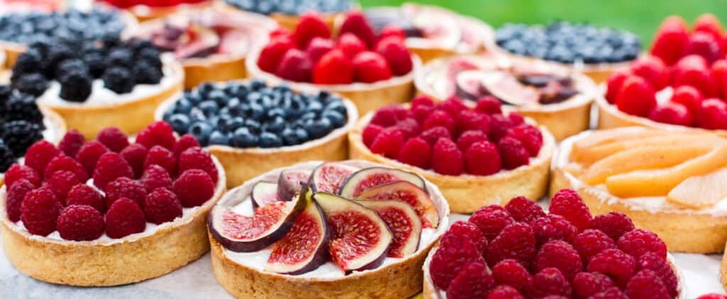 Colorful assortment of fresh fruit tarts topped with raspberries, blueberries, and figs showcasing fruit trends in bakery