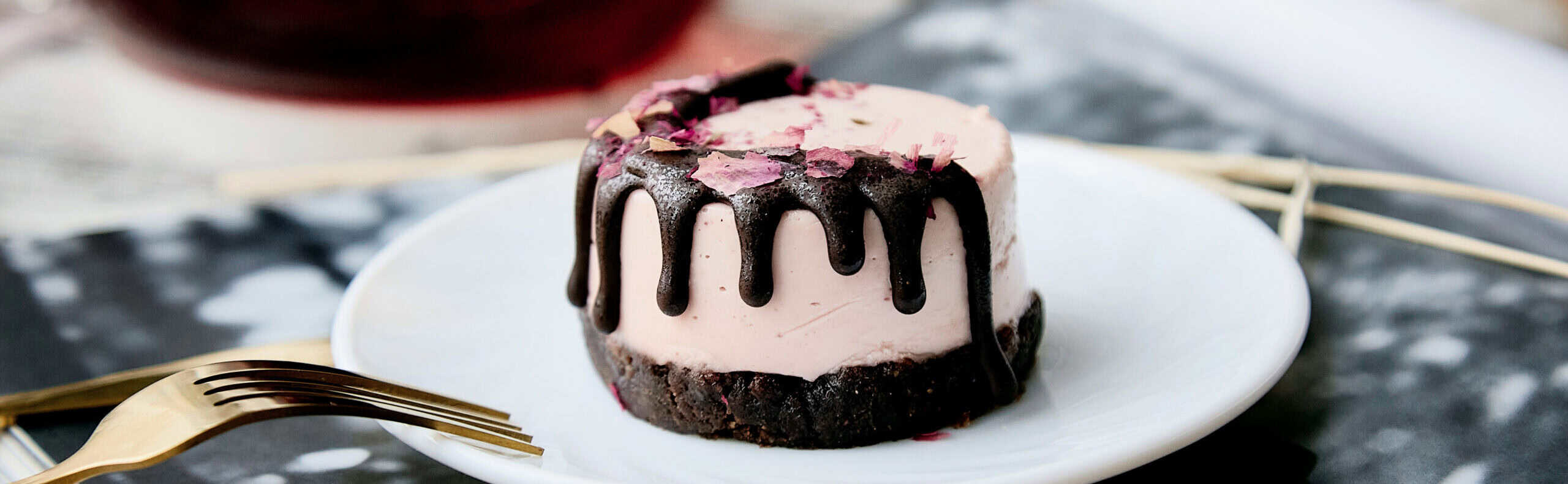 Elegant mini mousse cake with chocolate drip and edible rose petals served with hibiscus tea, showcasing premium fruit-forward bakery innovation