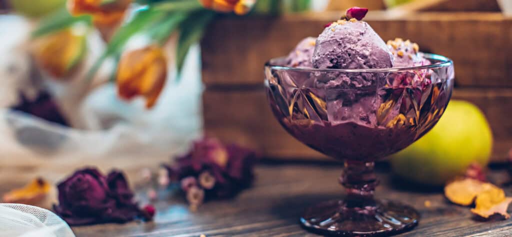 Beautiful lilac-colored ice cream scoop topped with roasted nuts and fresh edible flowers