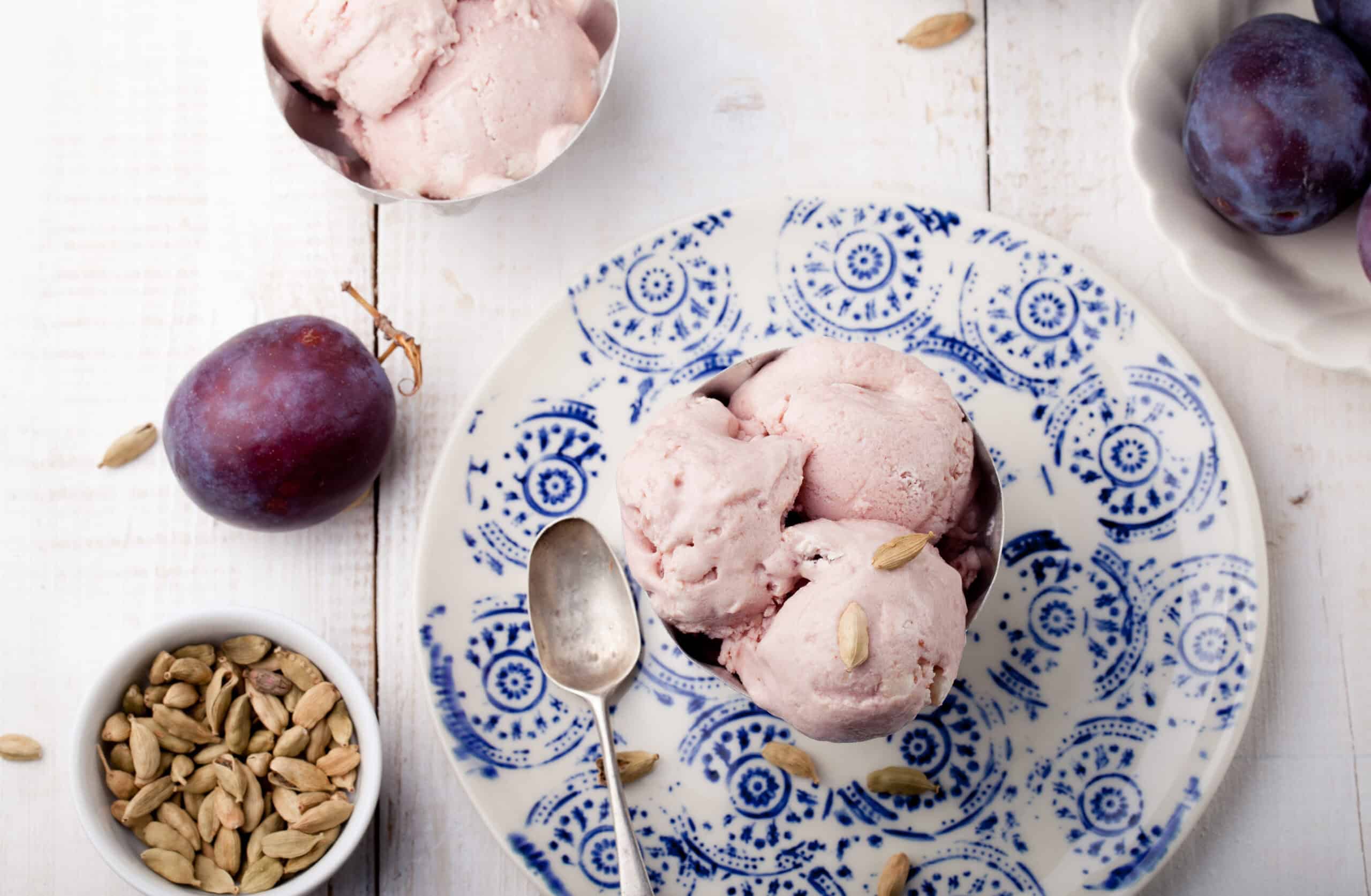 Soft plum-colored ice cream scoops topped with aromatic cardamom seeds on white background, functional spiced botanical