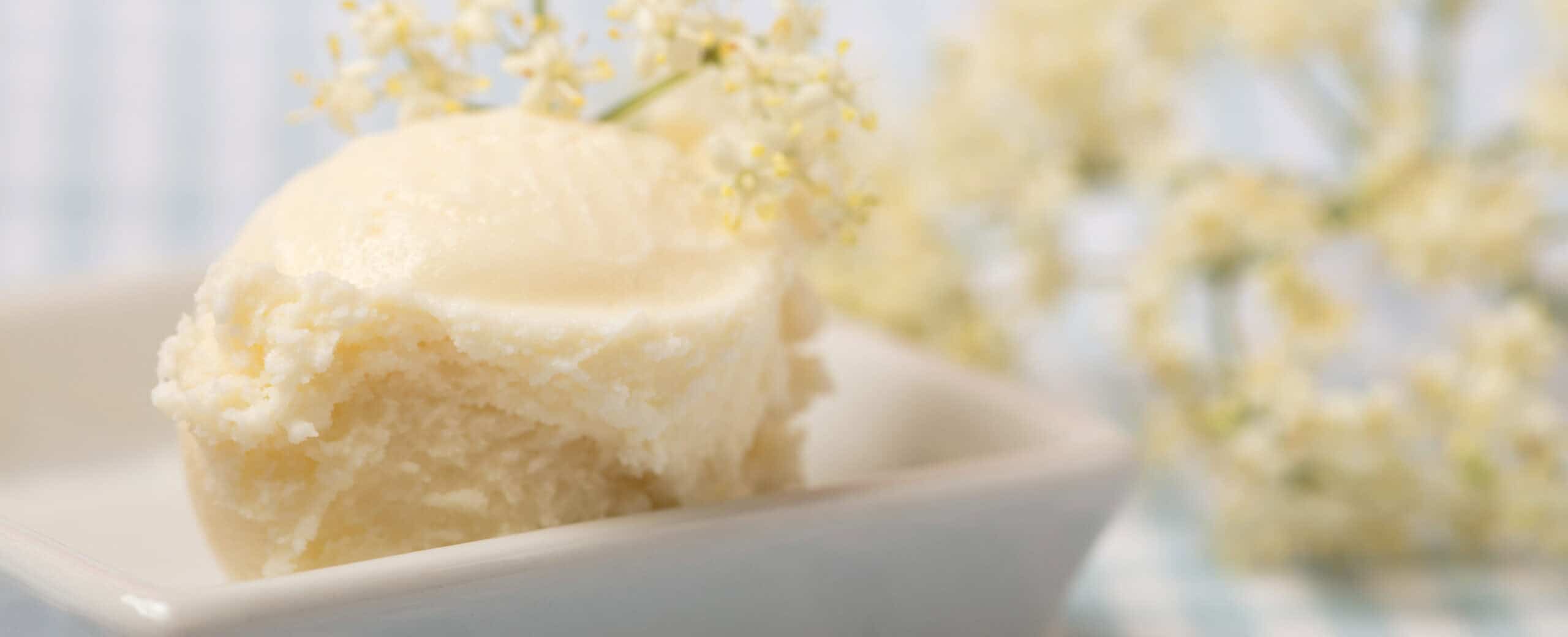 Creamy vanilla ice cream with delicate white elderflower blossoms and fresh green leaves, functional floral botanical