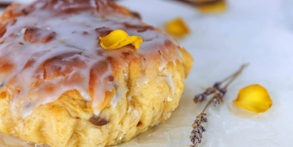 Still life of glazed easter bread on crinkled parchment with lavender sprigs and yellow petals on a white surface. Selective focus