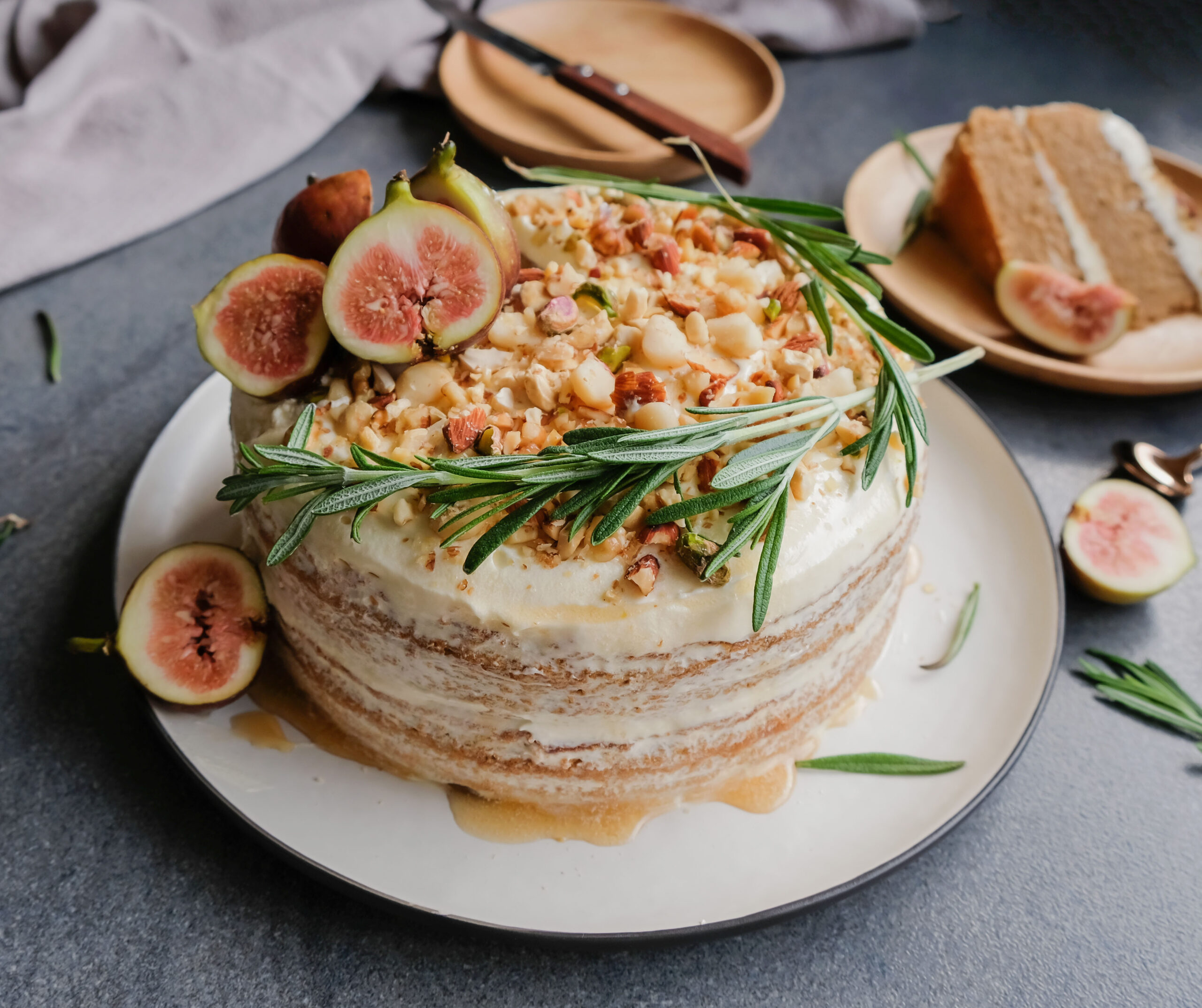 Naked layer cake topped with fresh figs, rosemary sprigs, and chopped pistachios, showcasing the versatility of botanical flavors in bakery.