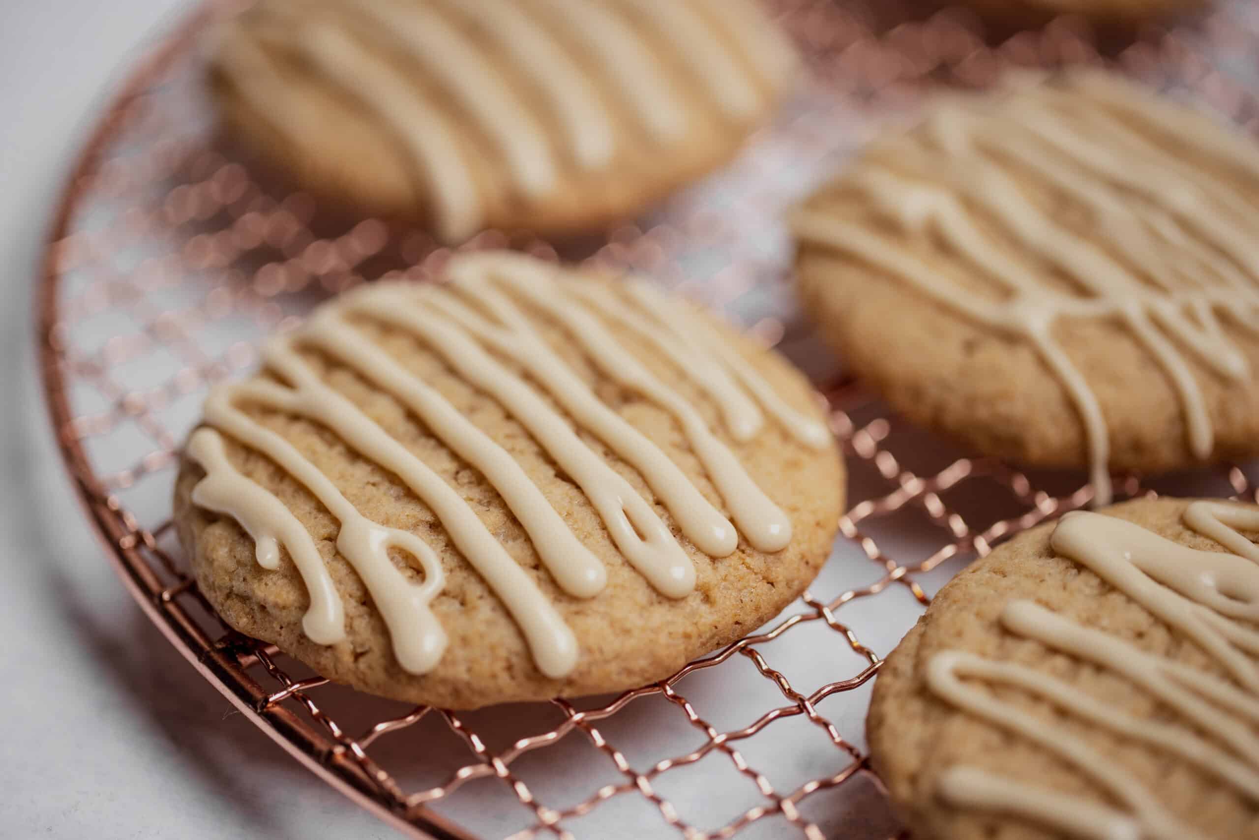 Spiced cookies with white glaze drizzle on a copper cooling rack, representing the application success of botanical flavors in bakery.