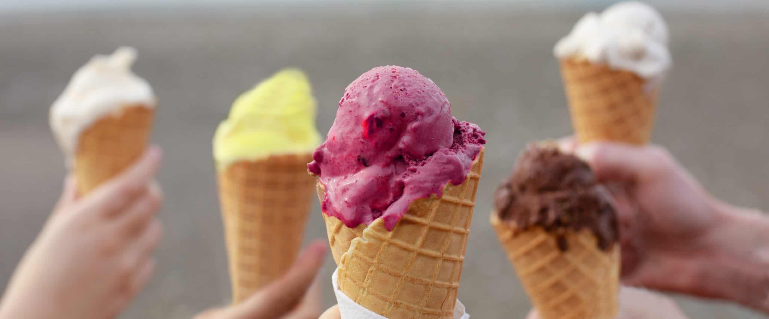 Assorted fruit-flavored ice cream cones held by hands, showcasing vibrant colors and textures.