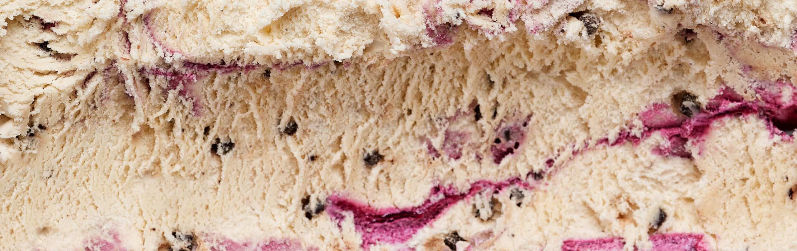Macro of a berry variegate ribbon swirled through cream ice cream with chocolate flecks — the texture challenge in functional ice cream formulation.