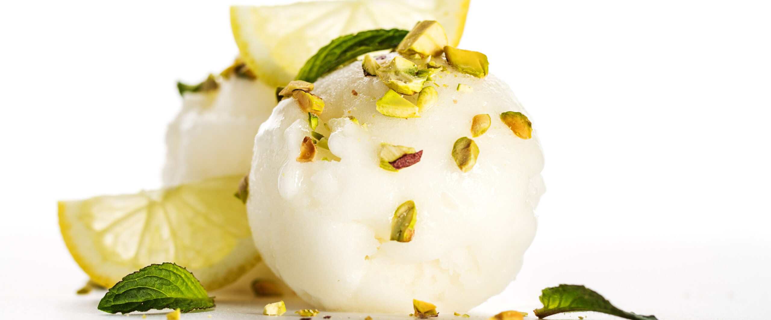 Lemon sorbet scoops topped with crushed pistachios, fresh mint, and lemon wedges — botanical ingredients adding flavor and textural complexity to ice cream.