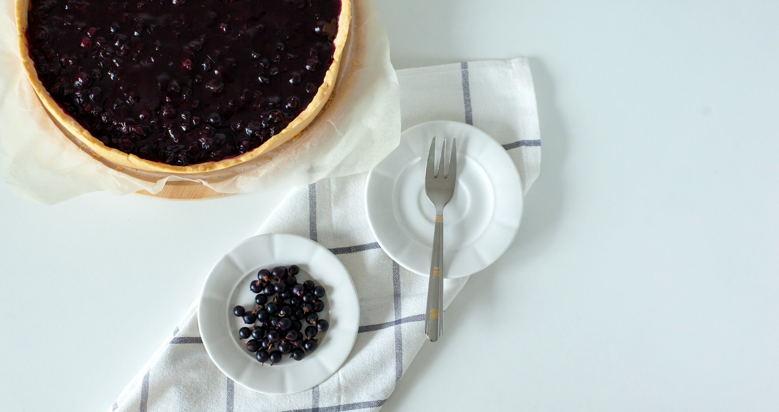 Overhead view of a whole blackcurrant tart on white with a napkin and fork, styled as a clean-label bake-stable fruit filling solution.