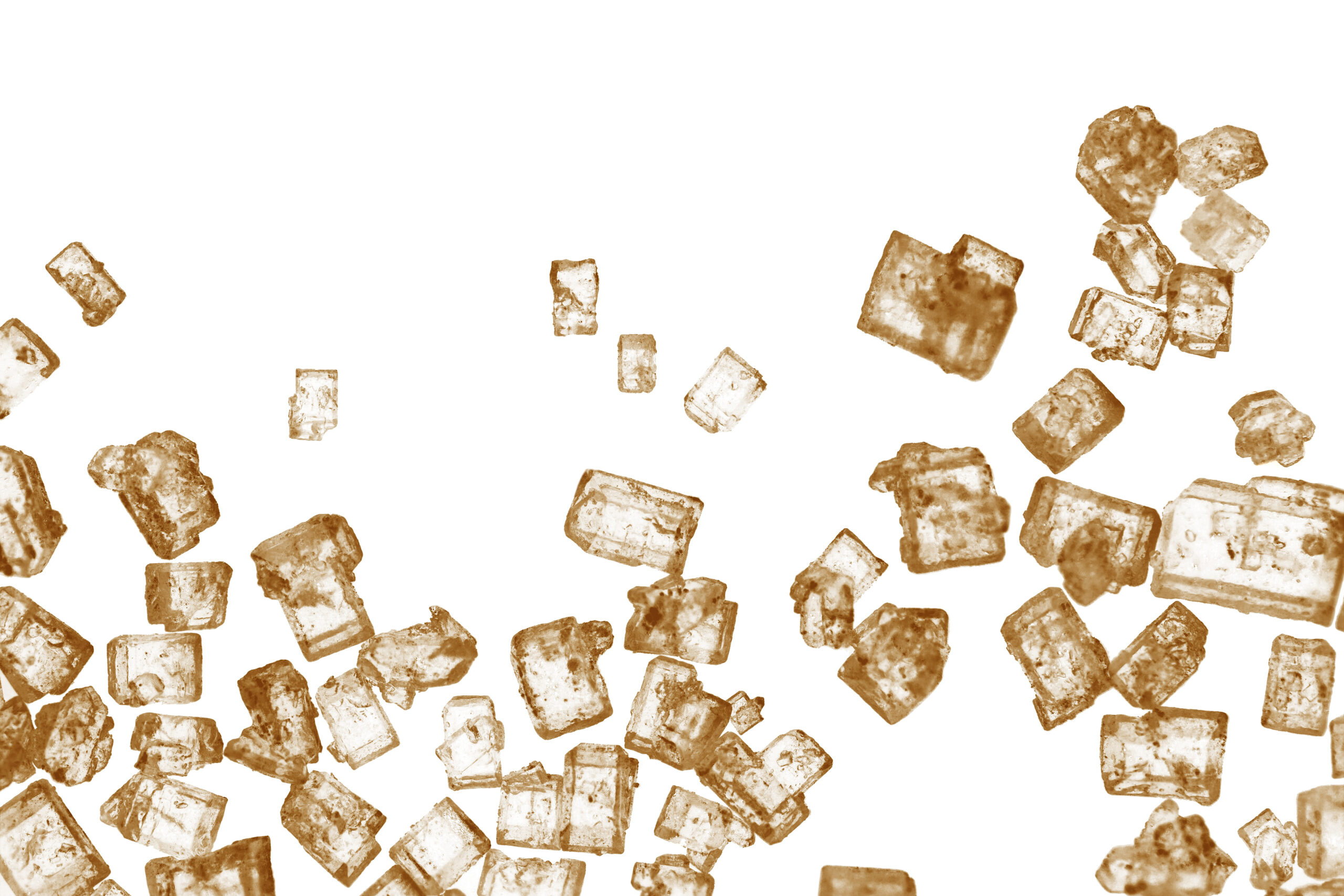 Macro of caramel-colored sugar crystals scattered on a white background, representing Brix and sugar's role in lowering water activity.