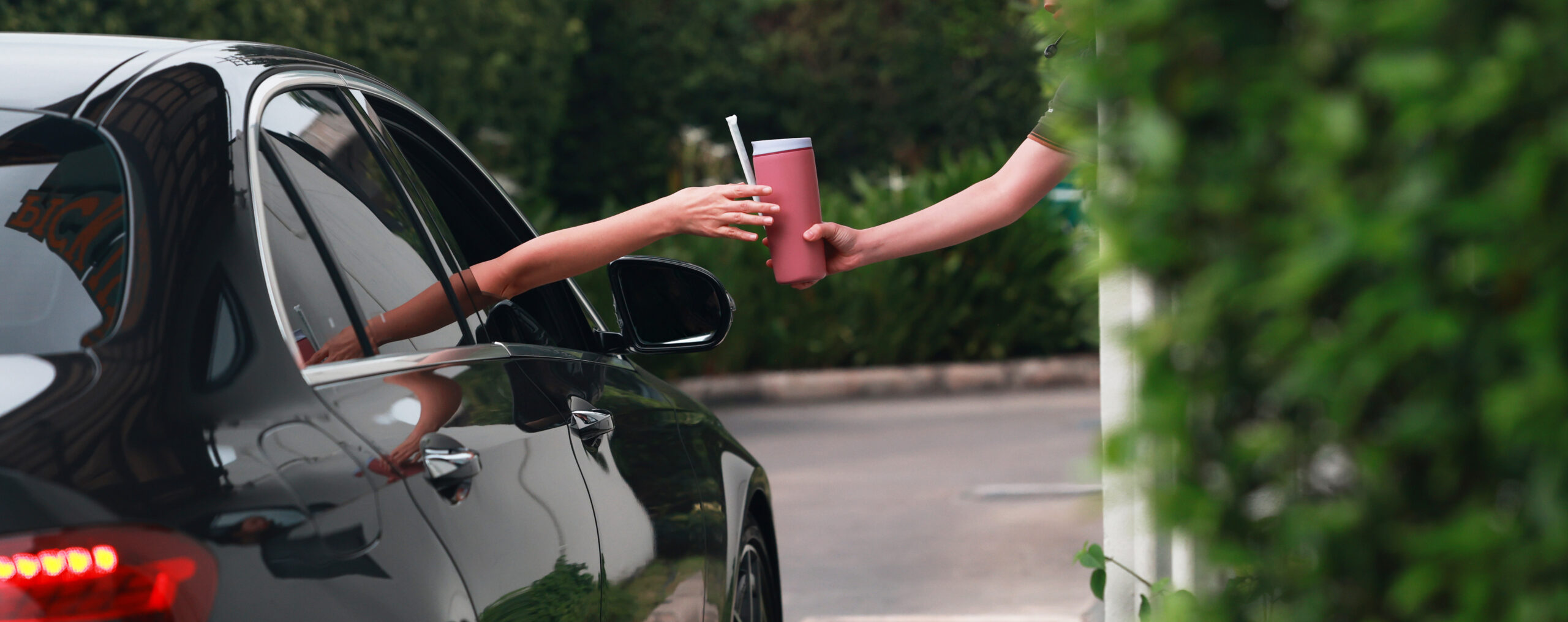 Employee handing a pink iced beverage to a driver at a drive-thru window