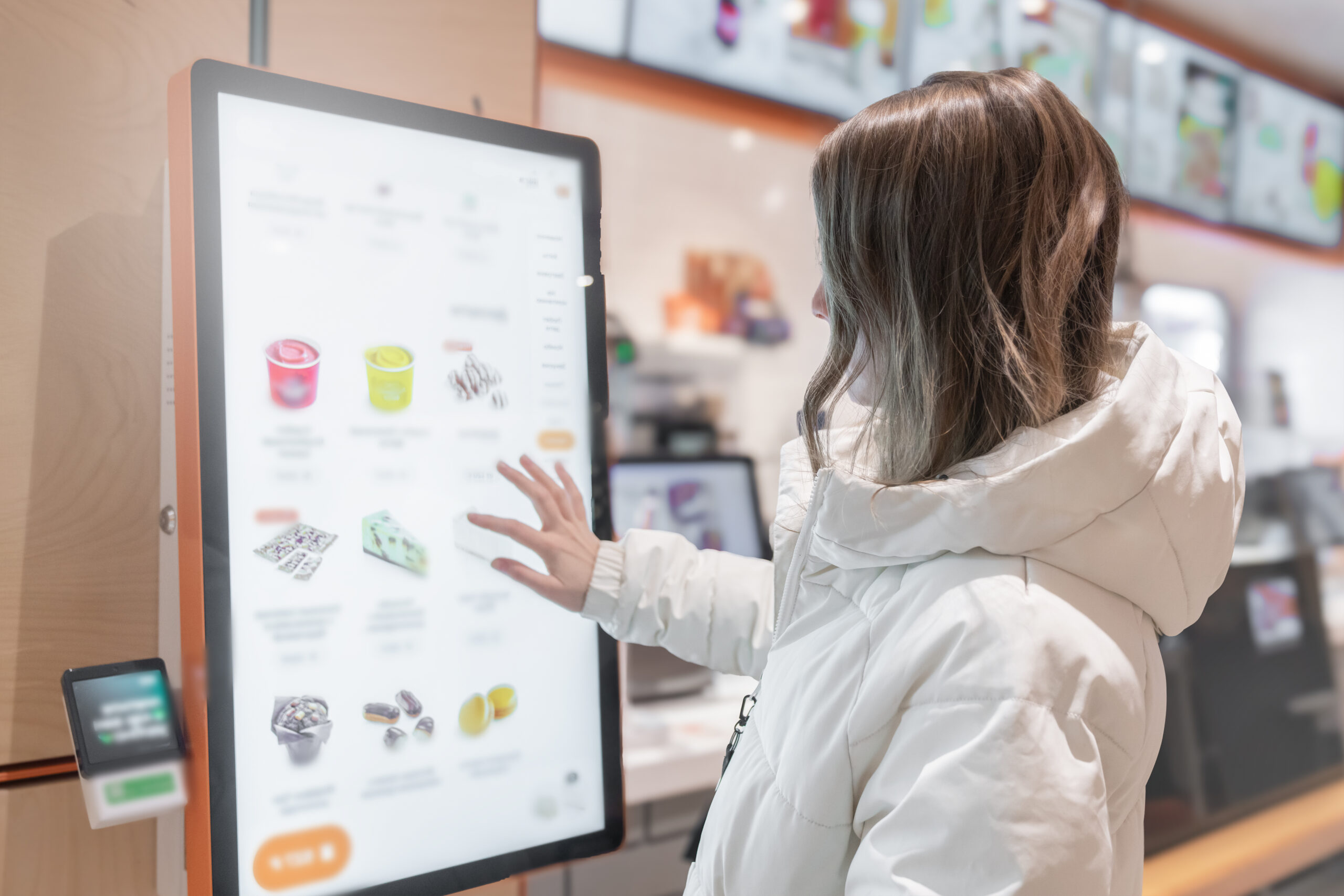 Customer ordering from a self-service touchscreen kiosk displaying drinks and desserts