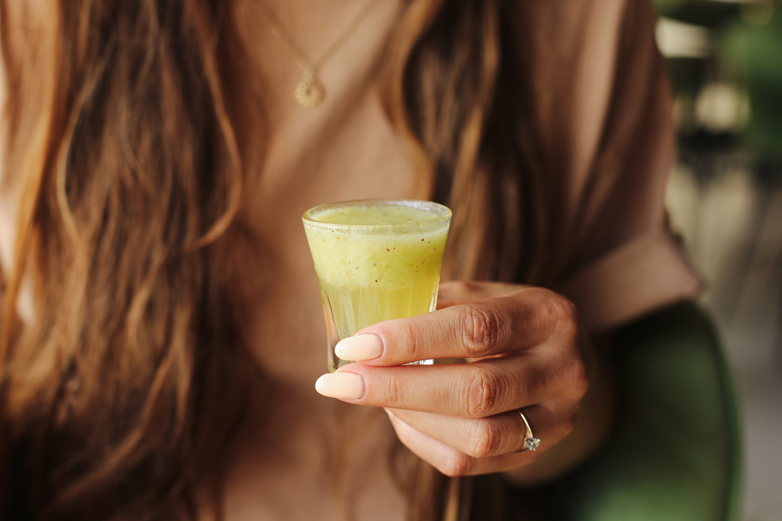 Woman holding a green wellness shot, one of the fastest-growing food service beverage trends