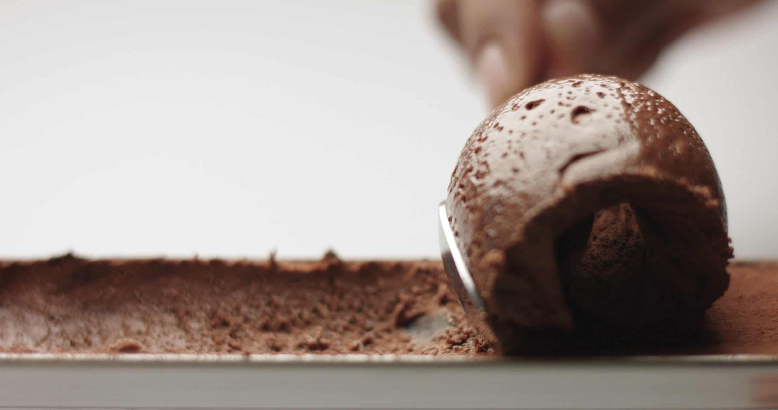 Chocolate ice cream scoop lifting from a tray dusted with cocoa powder