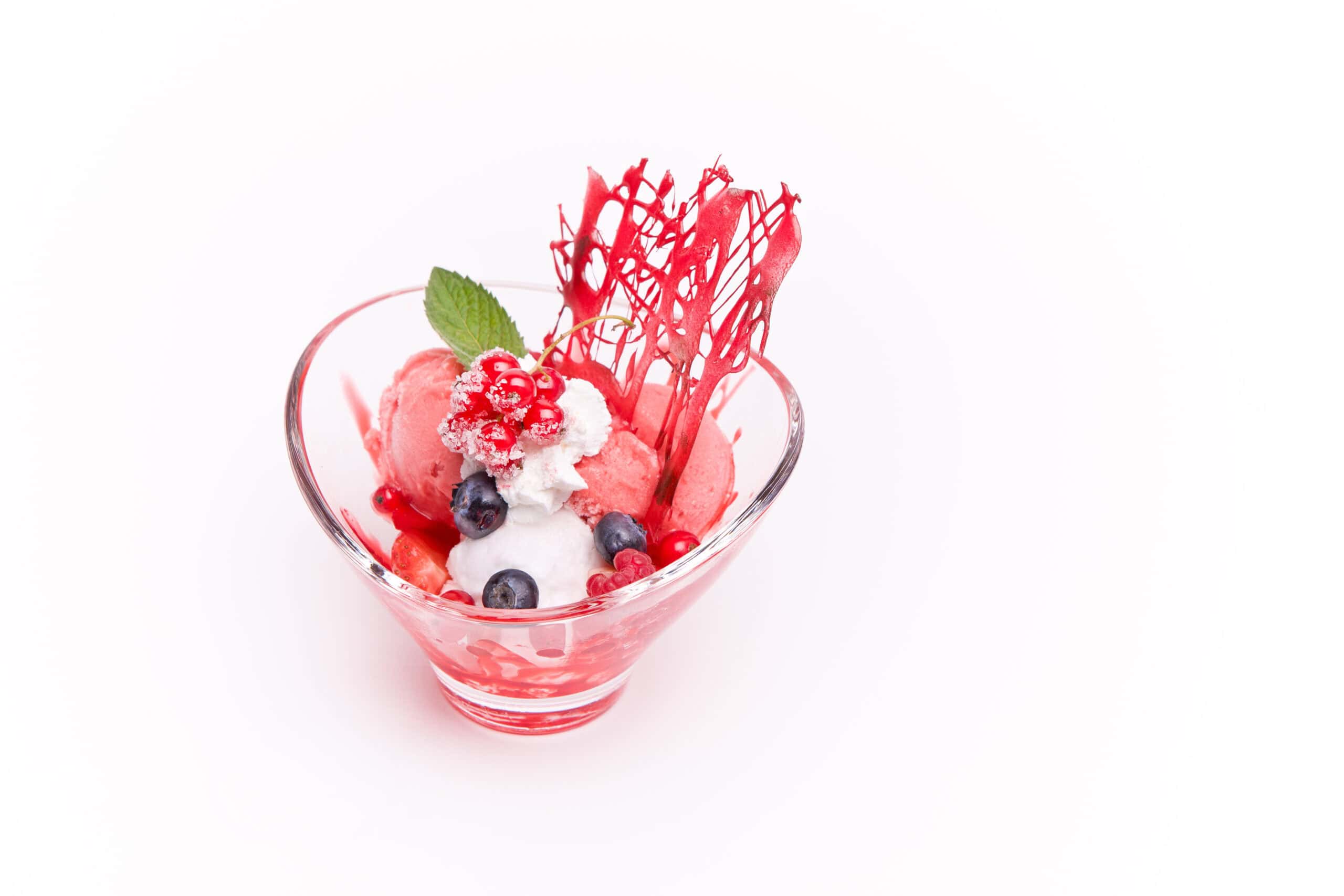 Pink berry sorbet and white scoops in a glass coupe with sugared red currants, blueberries, and a red sugar tuile