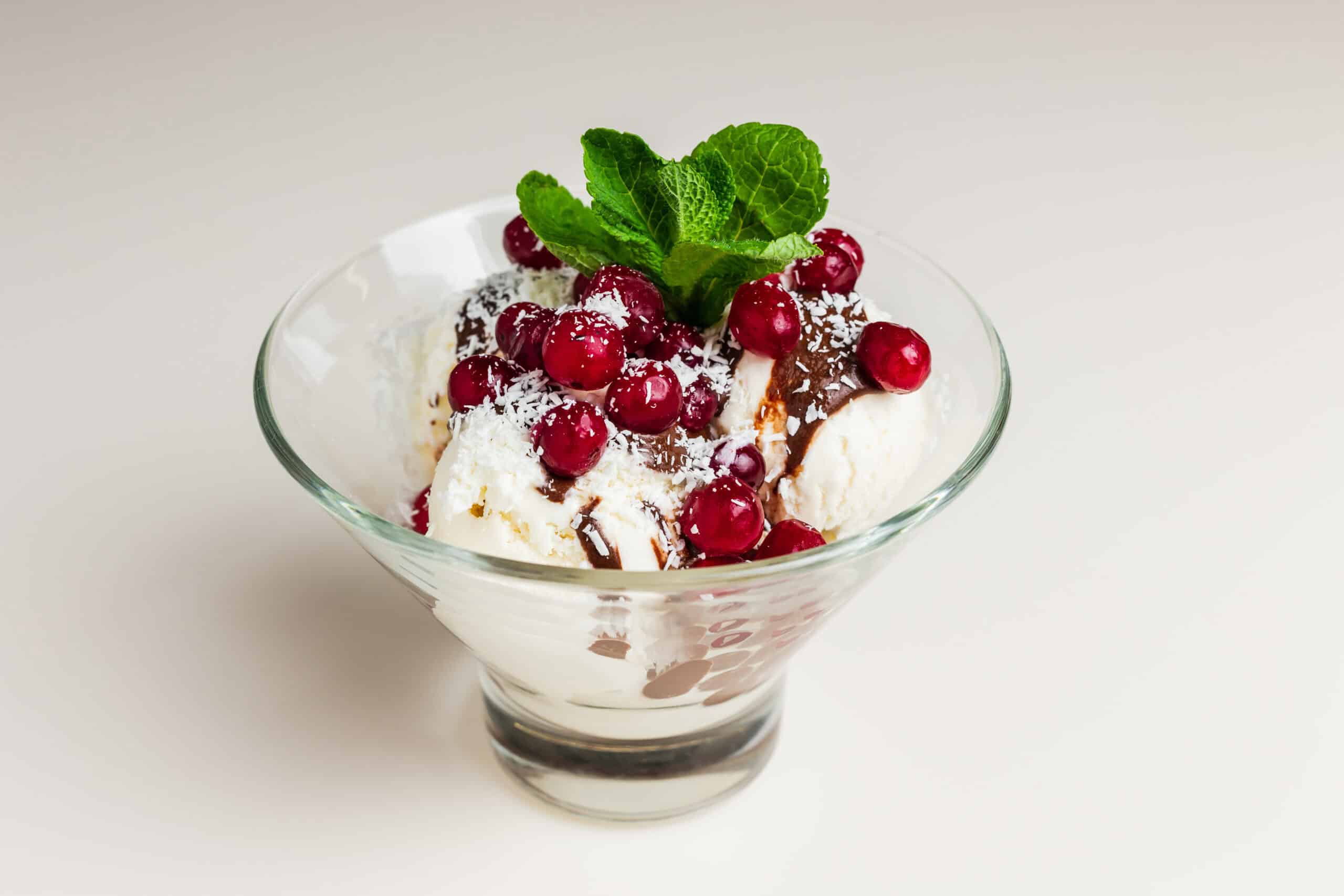 Vanilla ice cream scoops topped with cranberries, mint, chocolate sauce, and white shavings in a glass dish